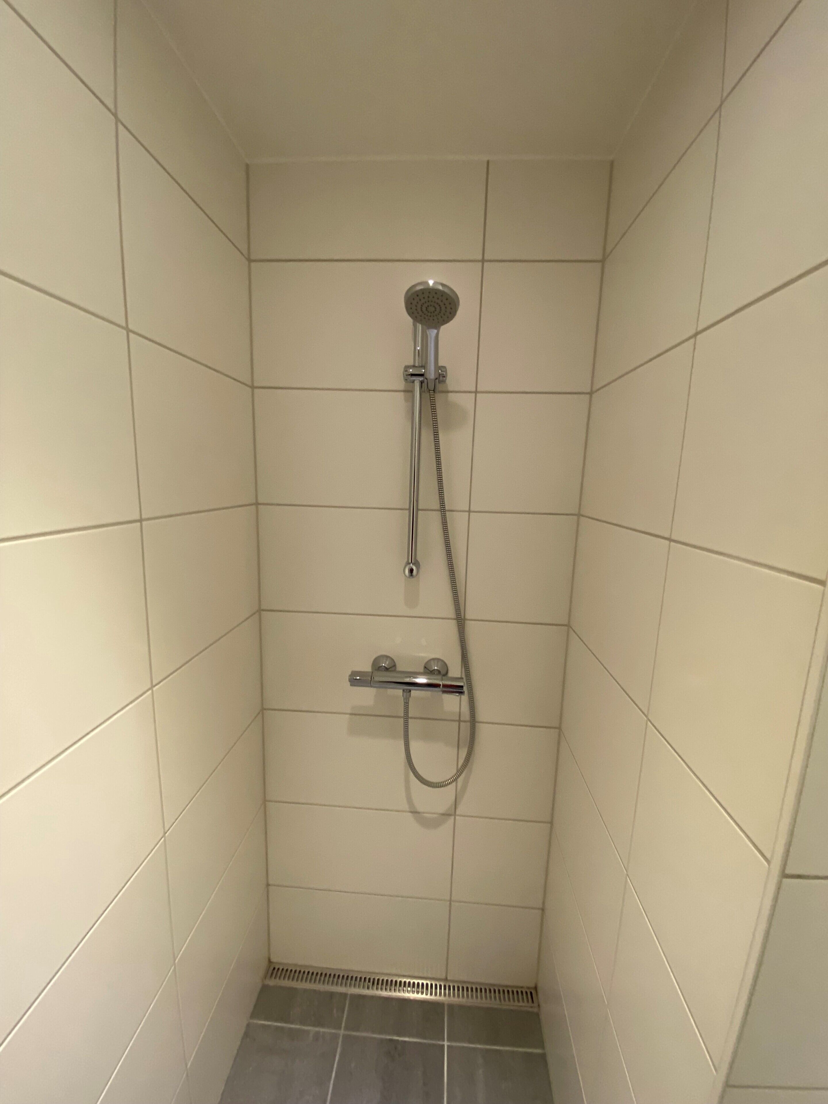 Un box de ducha pequeño con azulejos, equipado con un cabezal de ducha manual y un accesorio de ducha portátil.