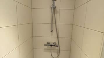 Un box de ducha pequeño con azulejos, equipado con un cabezal de ducha manual y un accesorio de ducha portátil.