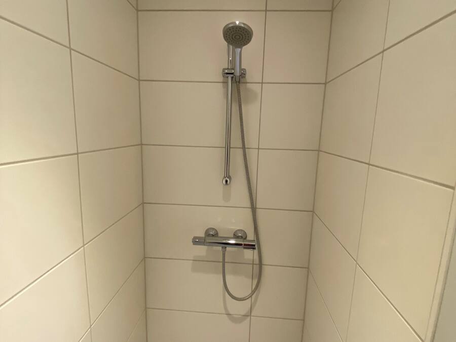 Un box de ducha pequeño con azulejos, equipado con un cabezal de ducha manual y un accesorio de ducha portátil.