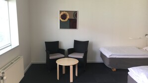 Une petite chambre d’hôtel avec deux chaises, une petite table, un lit et un tableau accroché au mur.
