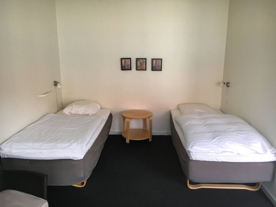 A room with two single beds, a small wooden stool, and three framed pictures on the wall.