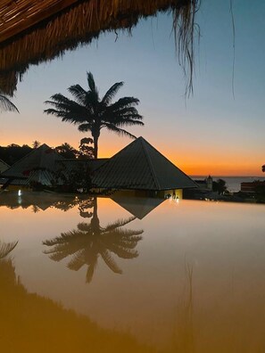 A tranquil evening at a resort with a clear sky, a calm pool reflecting palm trees, and a thatched-roof structure. - Hotel Morro de São Paulo (Cairu)
