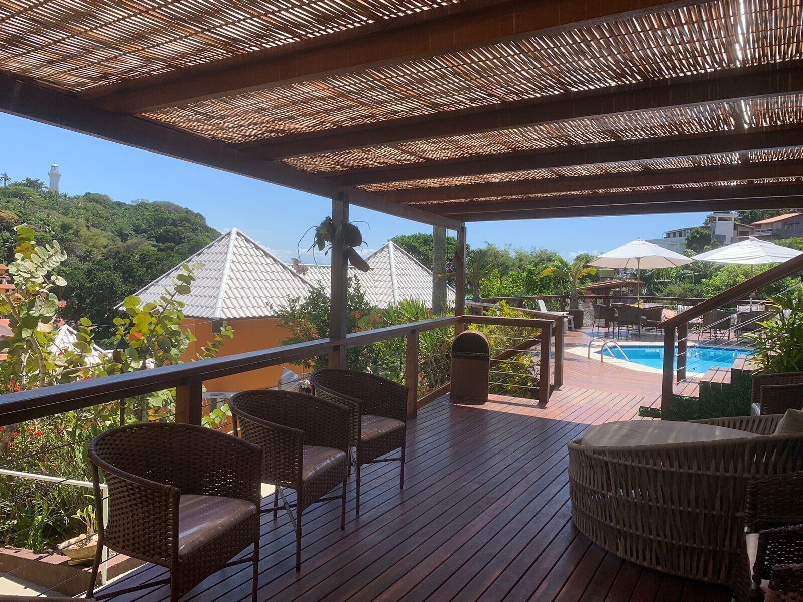 A wooden deck with wicker furniture overlooking a swimming pool and a view of buildings with tiled roofs.