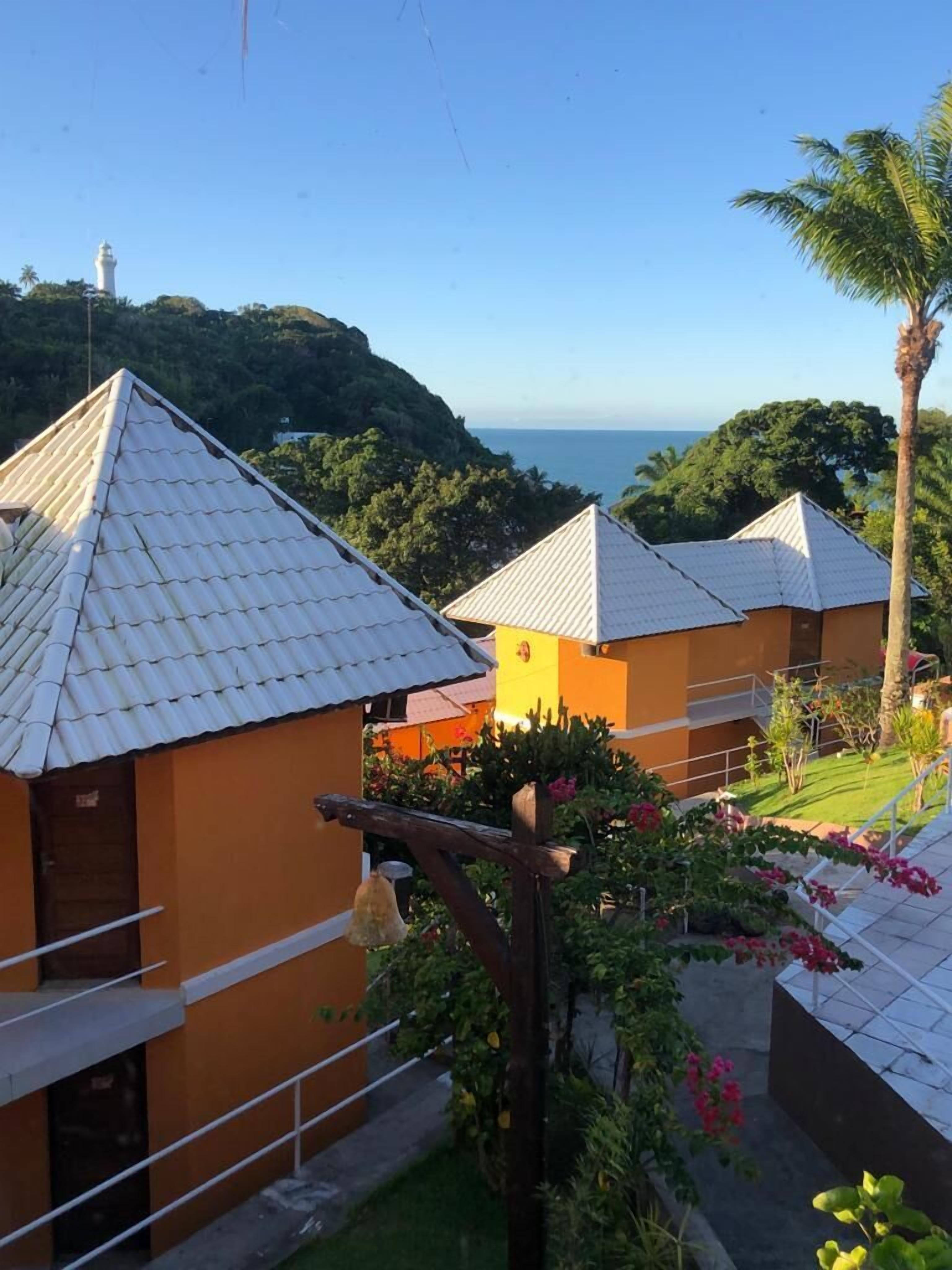 A coastal hotel with white tiled roofs, orange walls, and a view of the sea and a lighthouse.
