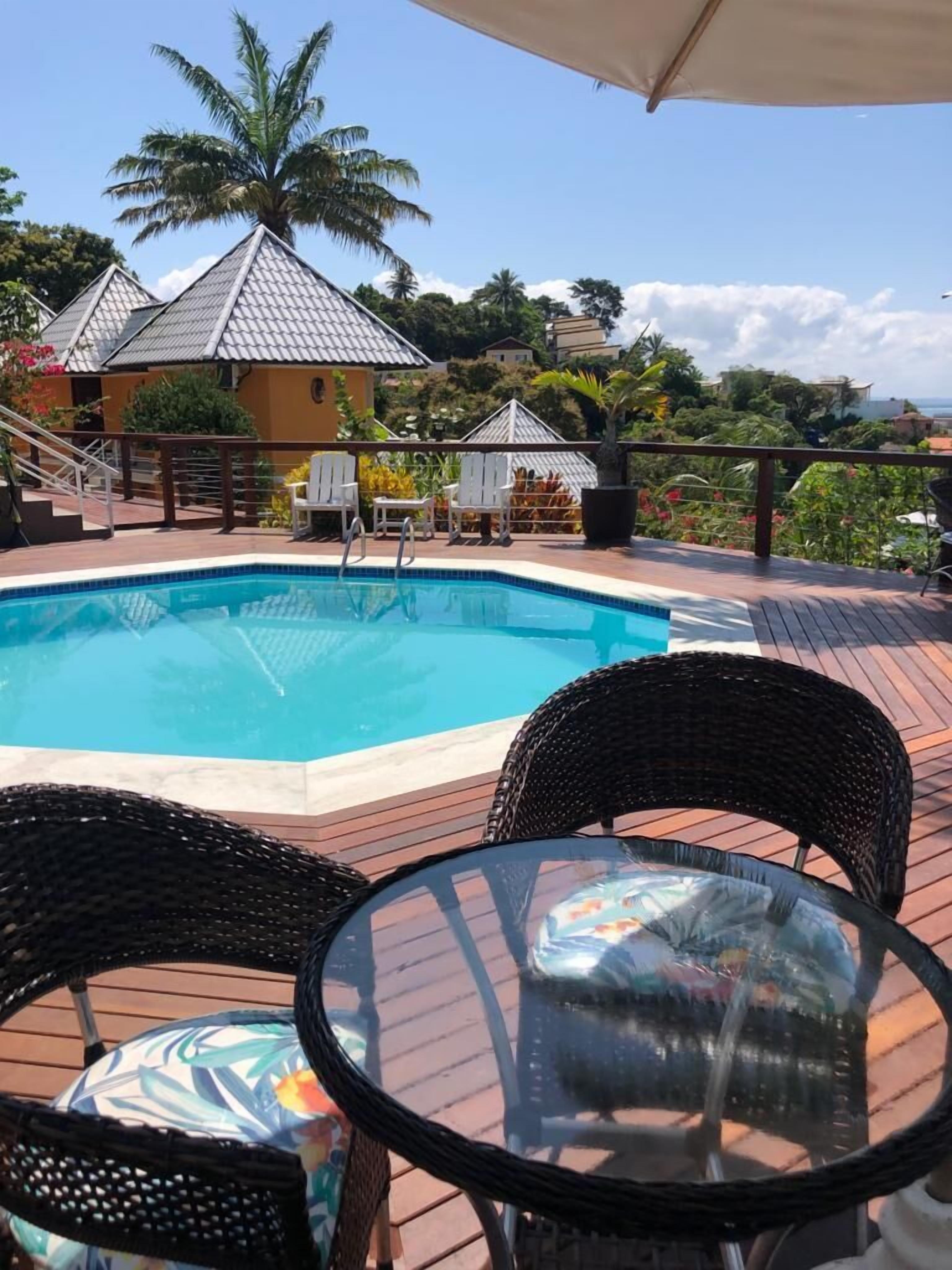 A swimming pool with a tiled deck, surrounded by lounge chairs and a covered area.