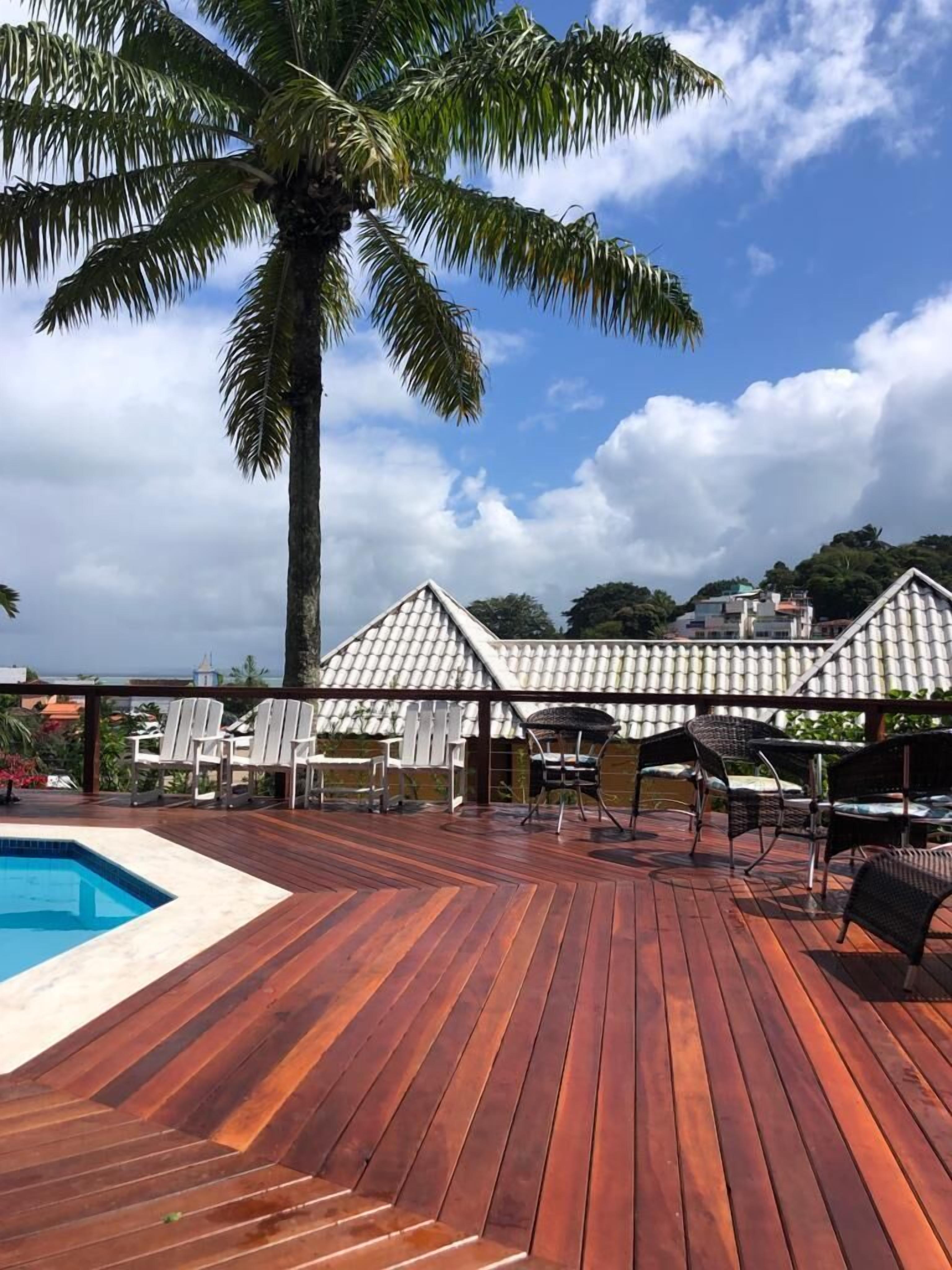 Una terraza de madera con piscina, sillas de descanso y una palmera.
