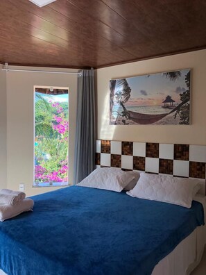 Une chambre d’hôtel avec un lit, une vue sur un paysage tropical et un tableau représentant une scène de plage accroché au mur.