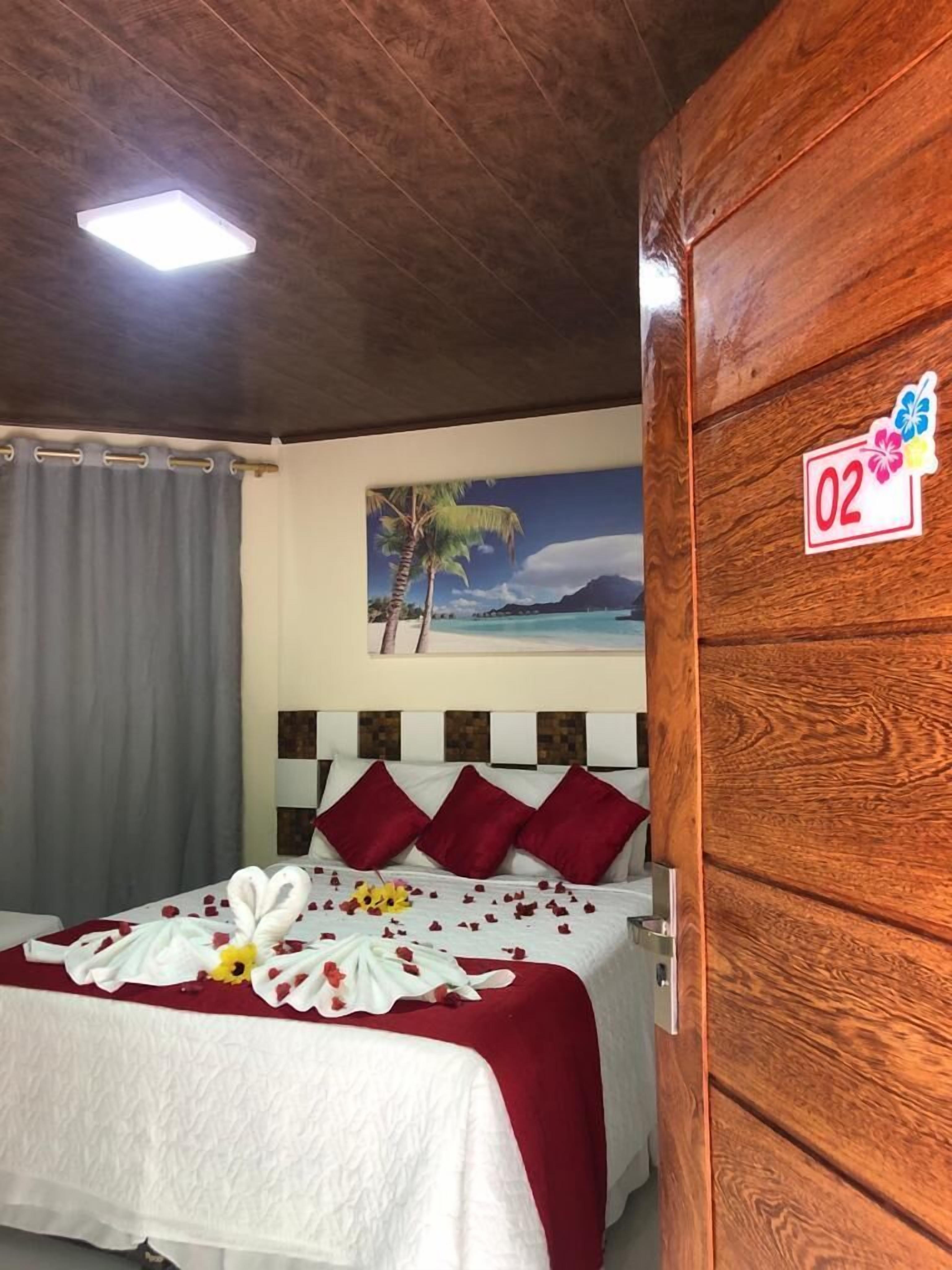 A hotel room with a wooden headboard, a bed with a white and red bedspread, and a painting of a beach scene on the wall.