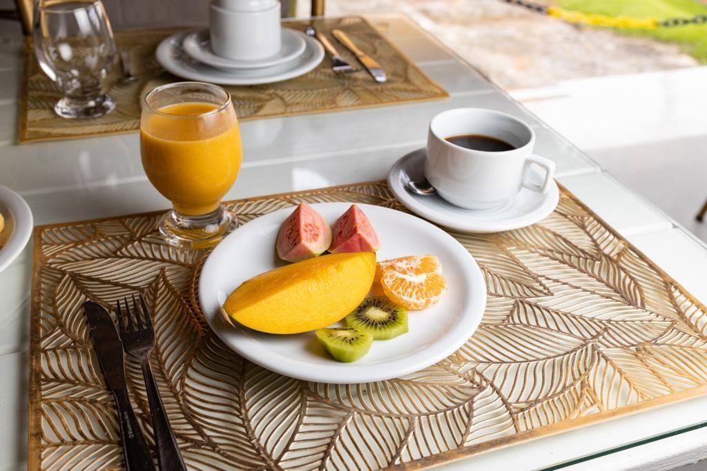 A breakfast setting with a plate of fruit, a glass of orange juice, and a cup of coffee on a table with a leaf-patterned placemat.