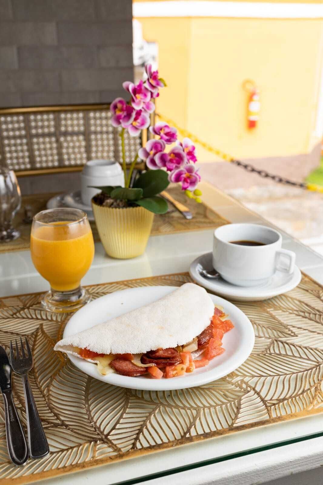 A breakfast setting with a plate of food, a cup of coffee, a glass of orange juice, and a potted orchid.