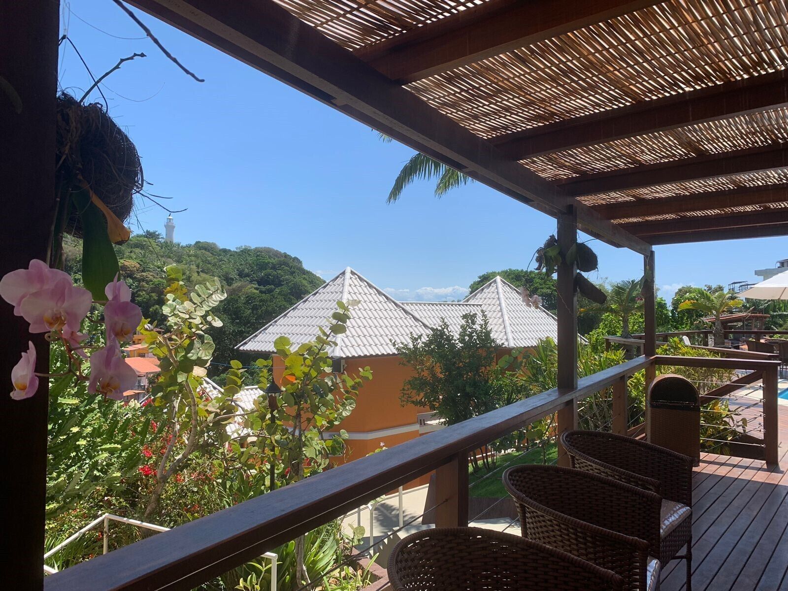 A balcony with wicker furniture, a view of buildings, and hanging orchids.