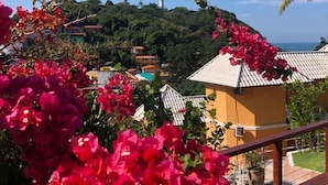 Una terraza de madera con flores rojas, vistas a una colina con edificios y un faro en la distancia.