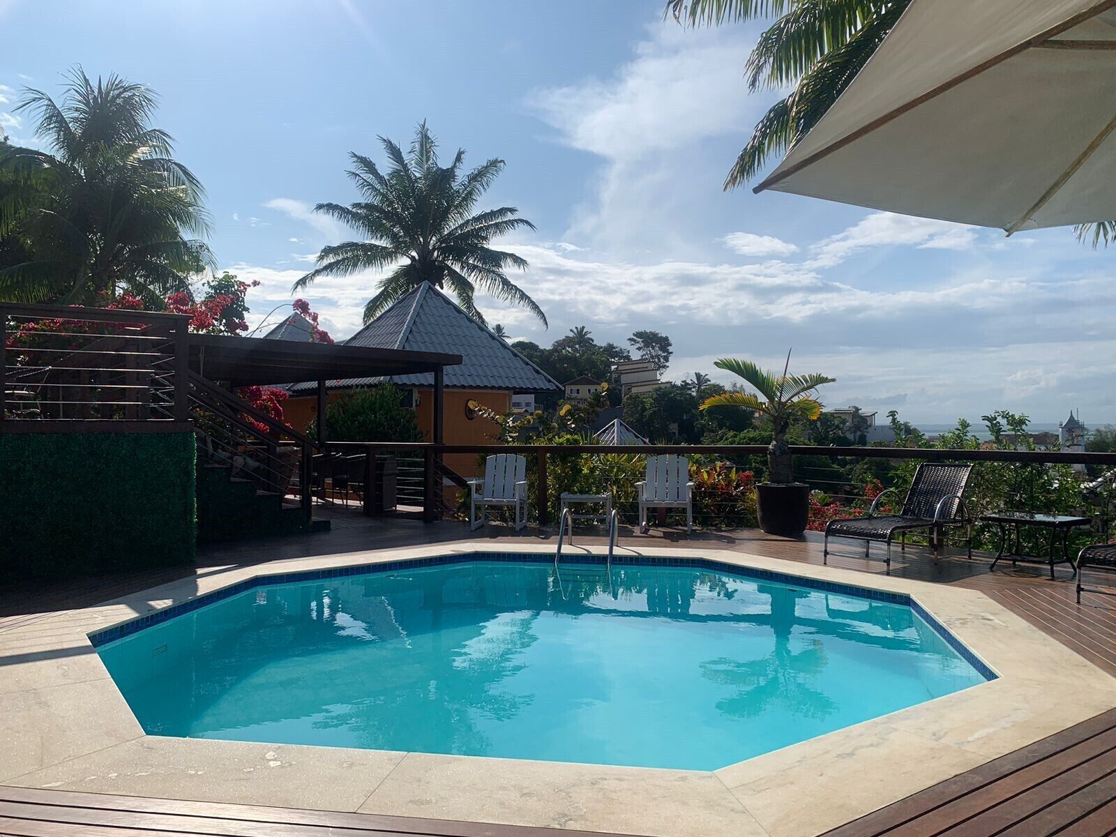 A swimming pool with a wooden deck, surrounded by palm trees and a gazebo.