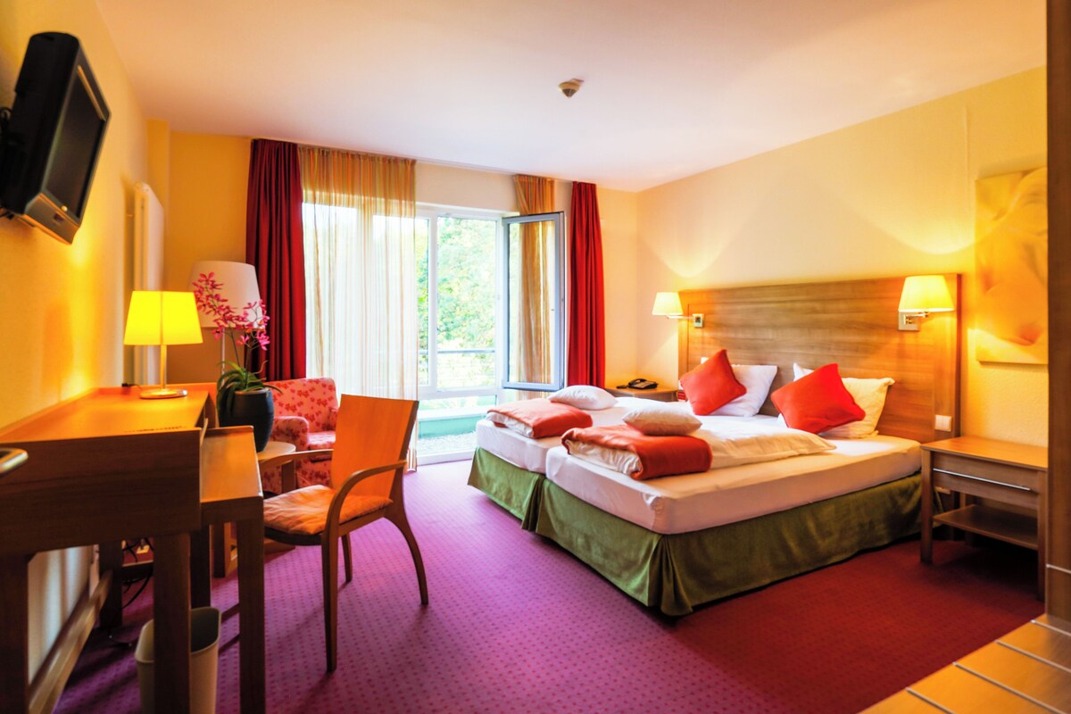 Une chambre d’hôtel avec deux lits, un bureau, une chaise, une télévision et une fenêtre avec des rideaux.