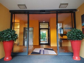 A hotel entrance with glass doors, a red mat, and two potted plants.