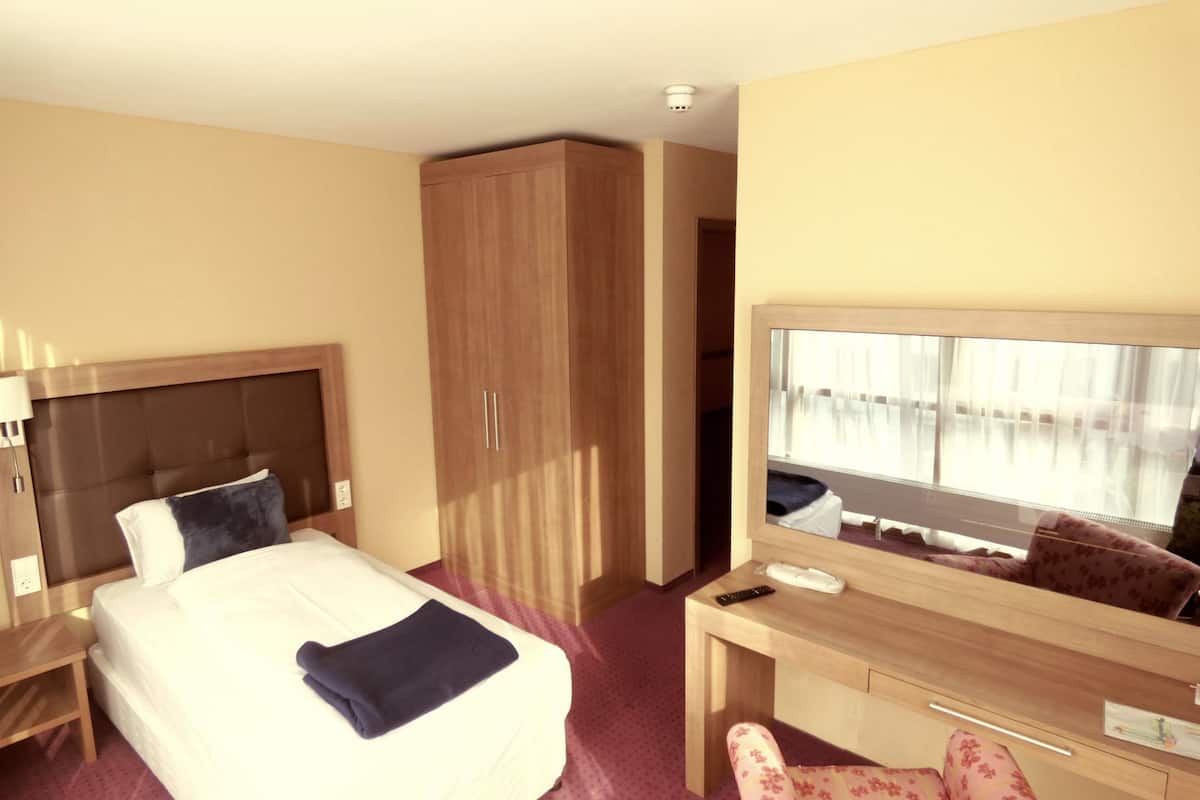 Une chambre d’hôtel équipée d’un lit, d’un bureau, d’une armoire et d’un grand miroir.