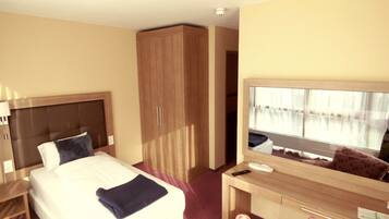 Habitación de hotel con cama, escritorio, armario y un espejo grande.