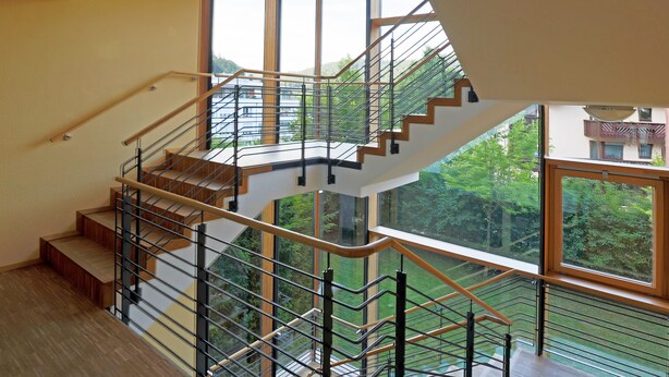 Un intérieur moderne avec un escalier en colimaçon, de grandes fenêtres et une vue sur la verdure environnante.