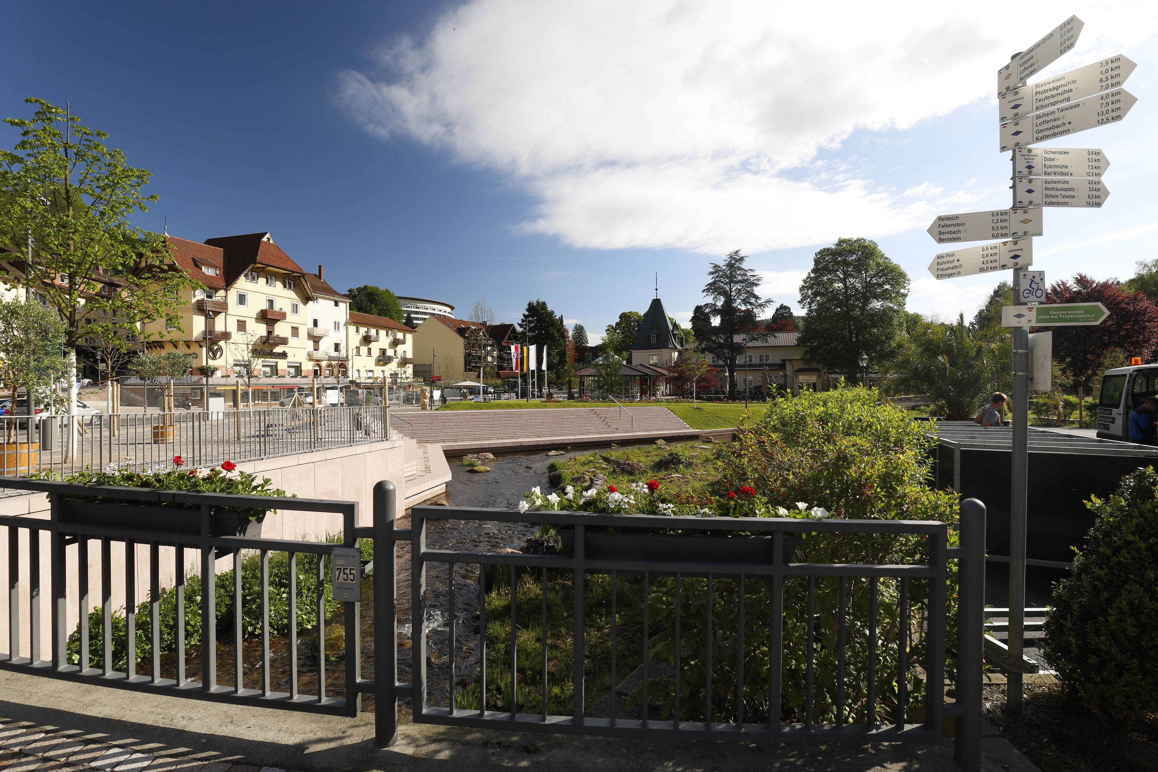 A town square with a directional signpost, a small canal, and buildings with balconies.
