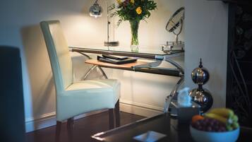 A modern office chair, a desk with a lamp, a vase with flowers, and a bowl of fruit.