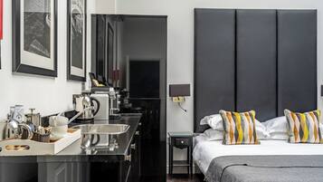 A modern hotel room with a large bed, a bedside table, a small desk with a kettle, and a large mirror.