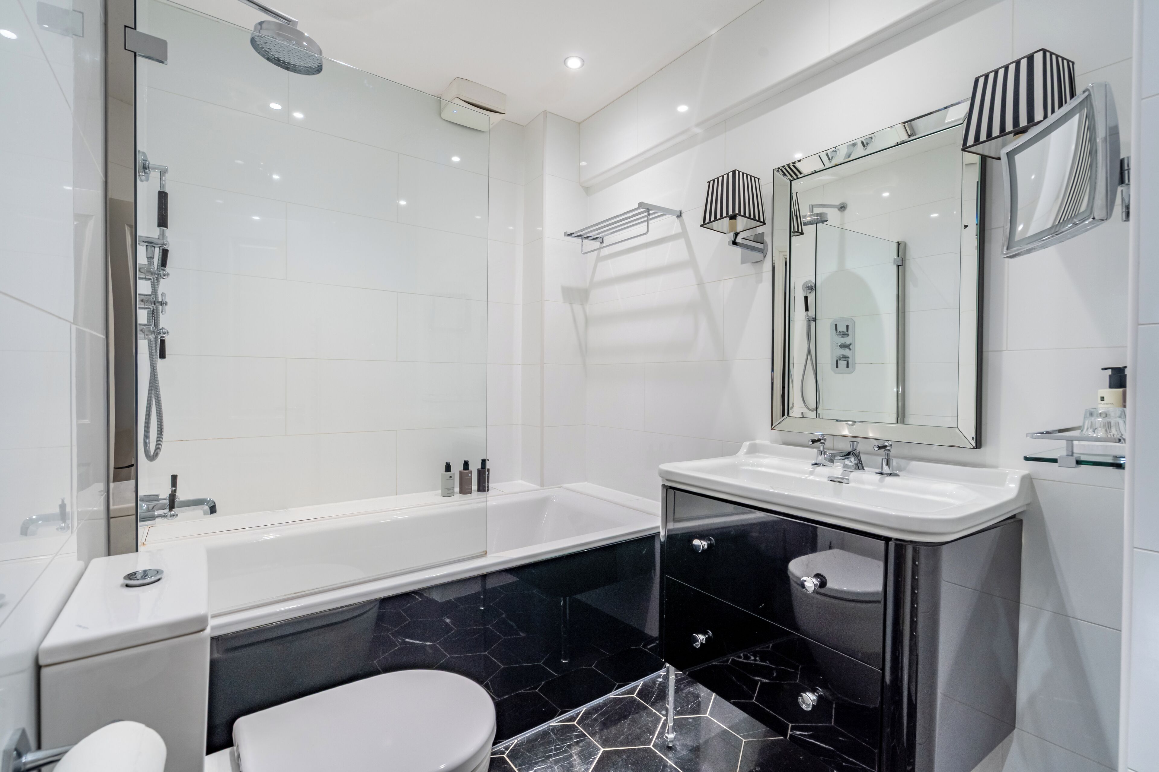 Een moderne badkamer met een douchecabine van glas, een witte badkuip, een zwart wastafelmeubel met spiegel en een wit toilet.