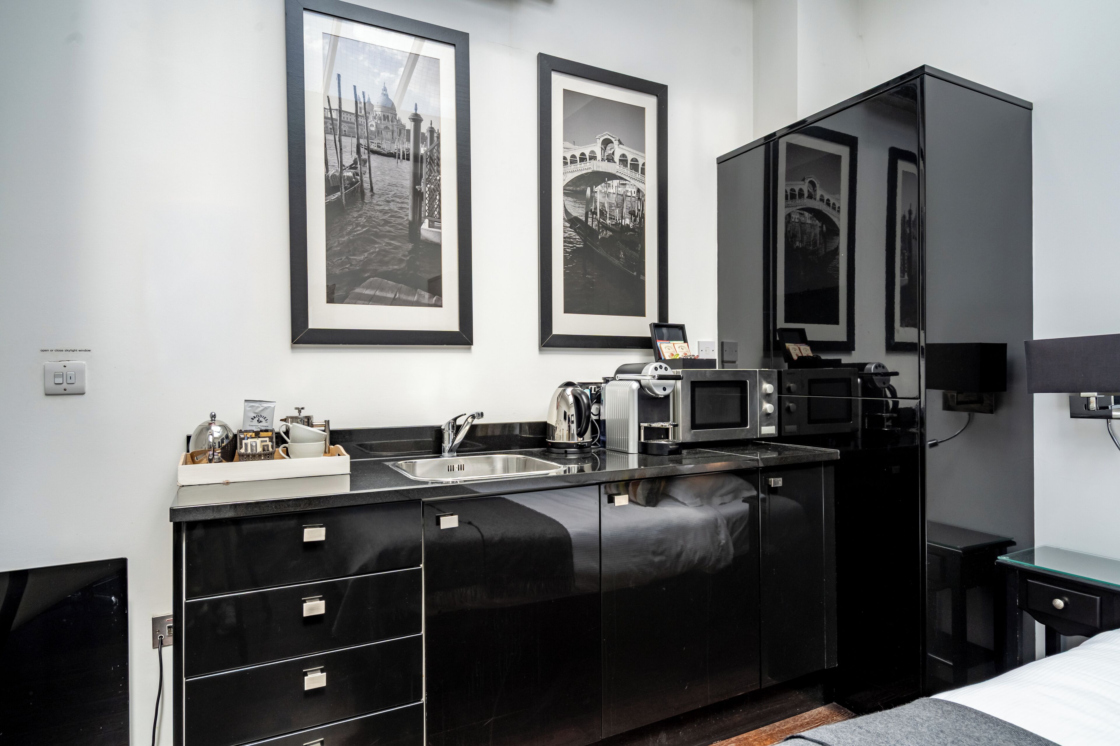 A modern kitchen with a black countertop, stainless steel appliances, and a sink. There are framed pictures on the wall above the counter.