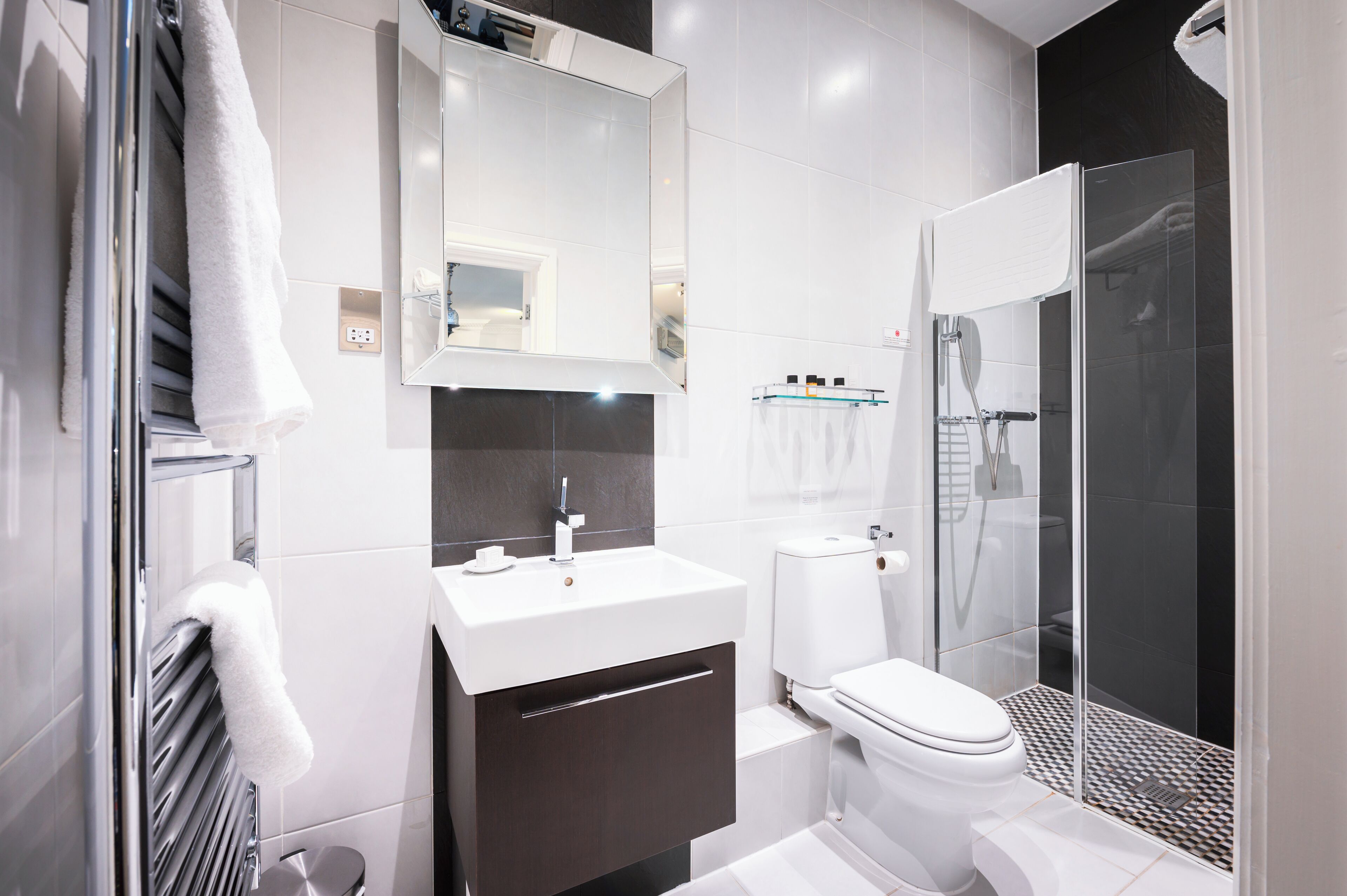 Un baño moderno con lavamanos blanco, tocador oscuro, inodoro y ducha con mampara de vidrio.