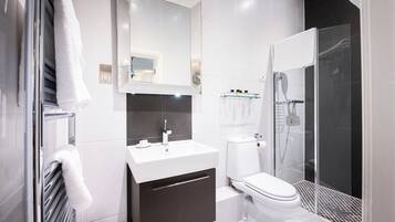 Un baño moderno con lavamanos blanco, tocador oscuro, inodoro y ducha con mampara de vidrio.