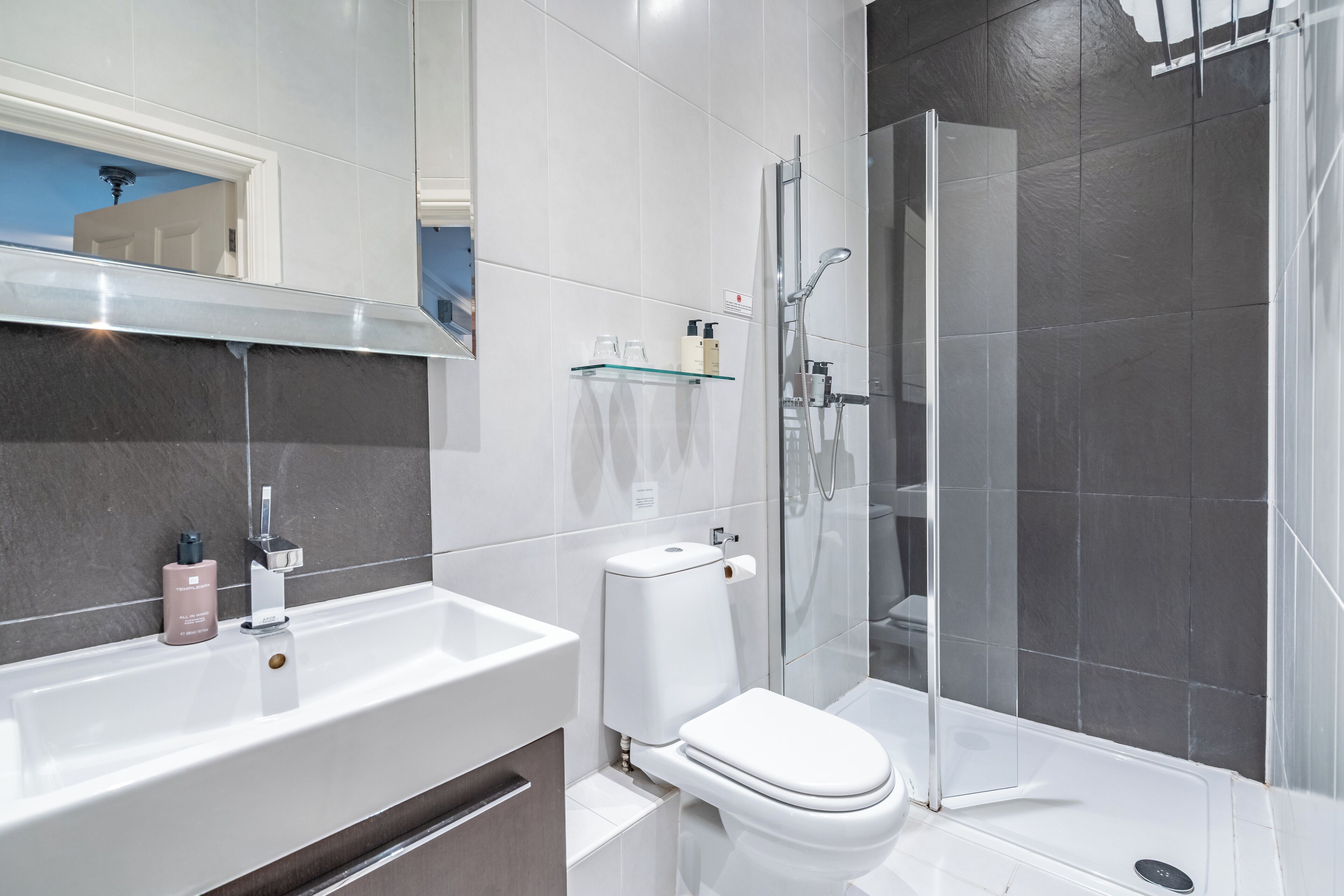 A modern bathroom with a white sink, a toilet, and a glass shower enclosure.