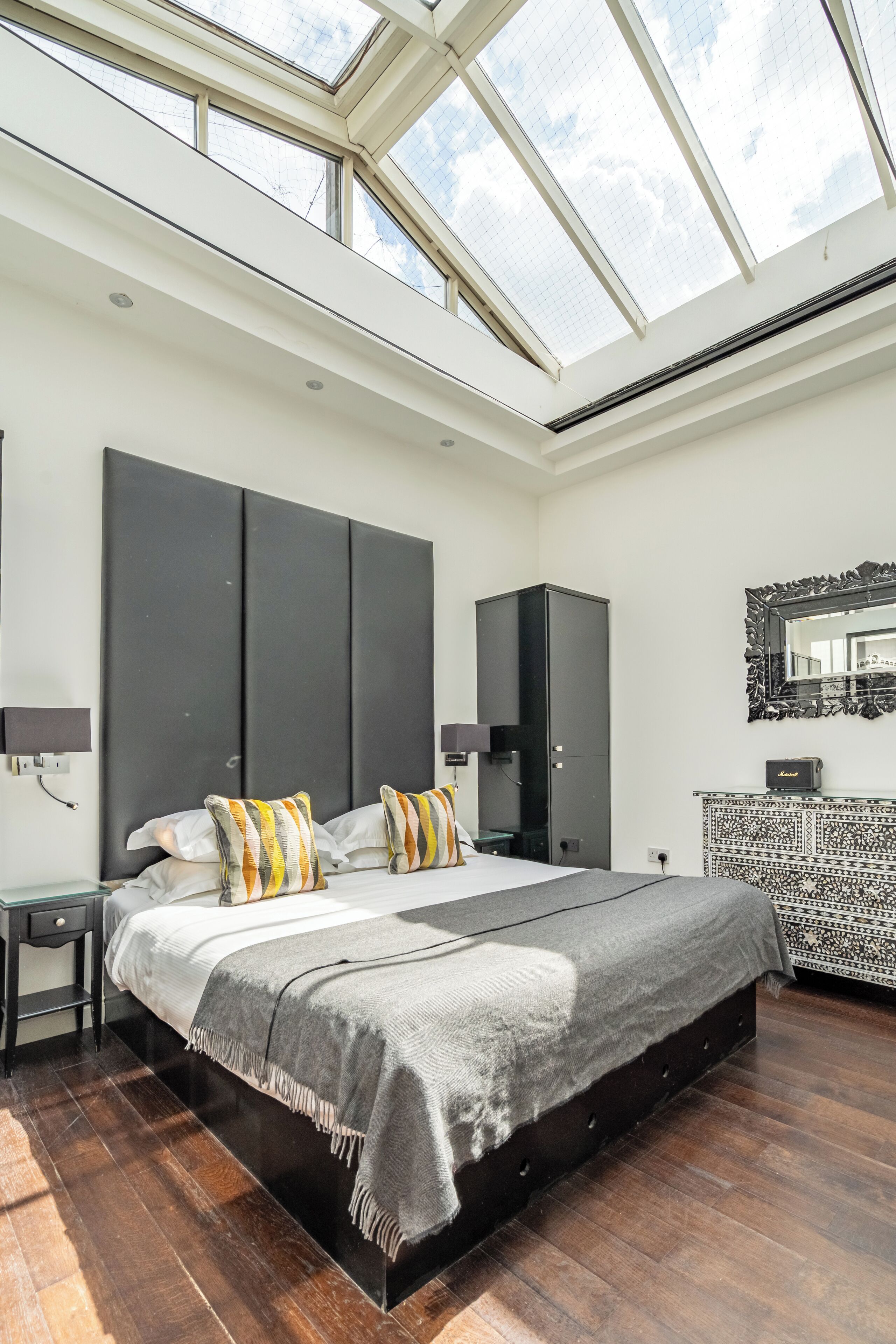 Een moderne slaapkamer met dakraam, een groot bed, een kledingkast en een console tafel met een patroon.