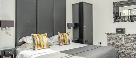 A modern bedroom with a skylight, a large bed, a wardrobe, and a patterned console table.