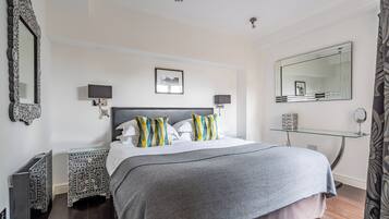 A neatly arranged bedroom with a large bed, two bedside tables, a glass shelf, and a mirror.