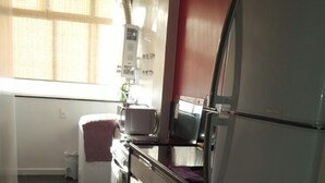 A compact kitchen with a refrigerator, stove, and a window with blinds. - Etours - Lindo 2 Quartos no Coração de Ipanema (Rio de Janeiro)