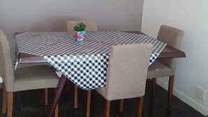 A dining area with a checkered tablecloth, four chairs, a small potted plant, and a violin on the wall. - Etours - Lindo 2 Quartos no Coração de Ipanema (Rio de Janeiro)