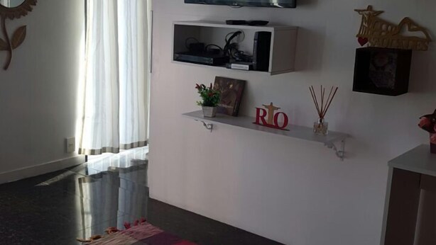 A modern living room with a flat-screen TV mounted on the wall, a patterned rug, and a small shelf with decorative items. - Etours - Lindo 2 Quartos no Coração de Ipanema (Rio de Janeiro)