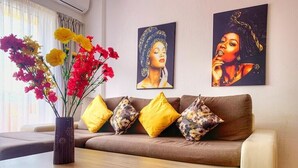 Una sala de estar con un sofá marrón, cojines amarillos y estampados florales, una mesa de centro de madera y un jarrón con flores.