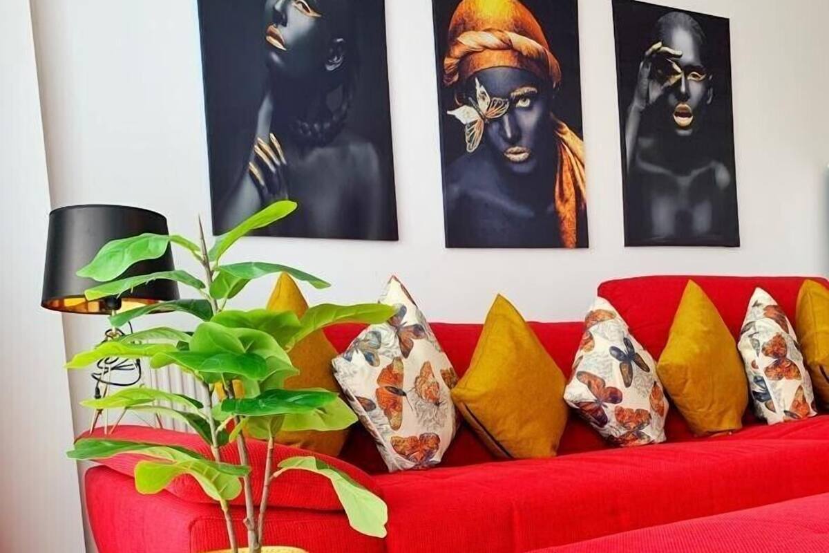 Un moderno salón con un sofá rojo, cojines decorativos, una planta en maceta y tres cuadros en la pared.