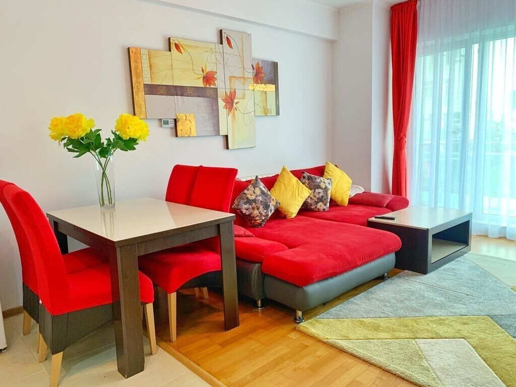 En moderne stue med en rød sofa, et spisebord med røde stole og en vase med gule blomster.