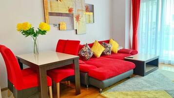 En moderne stue med en rød sofa, et spisebord med røde stole og en vase med gule blomster.