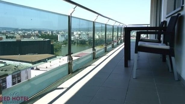 Balcón con barandilla de vidrio con vista a un paisaje urbano.