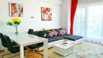 A modern living room with a white sofa, black chairs, a white coffee table, and a colorful rug. There are two paintings on the wall and a vase with yellow flowers on the table.