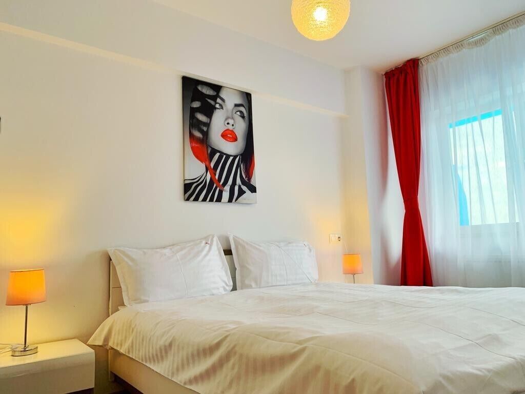 A hotel room with a bed, two bedside lamps, a painting on the wall, and a window with curtains.