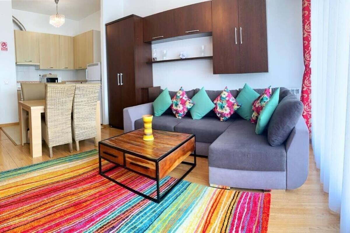 Una sala de estar moderna con un sofá gris, almohadones coloridos, una mesa de centro de madera y una alfombra a rayas.