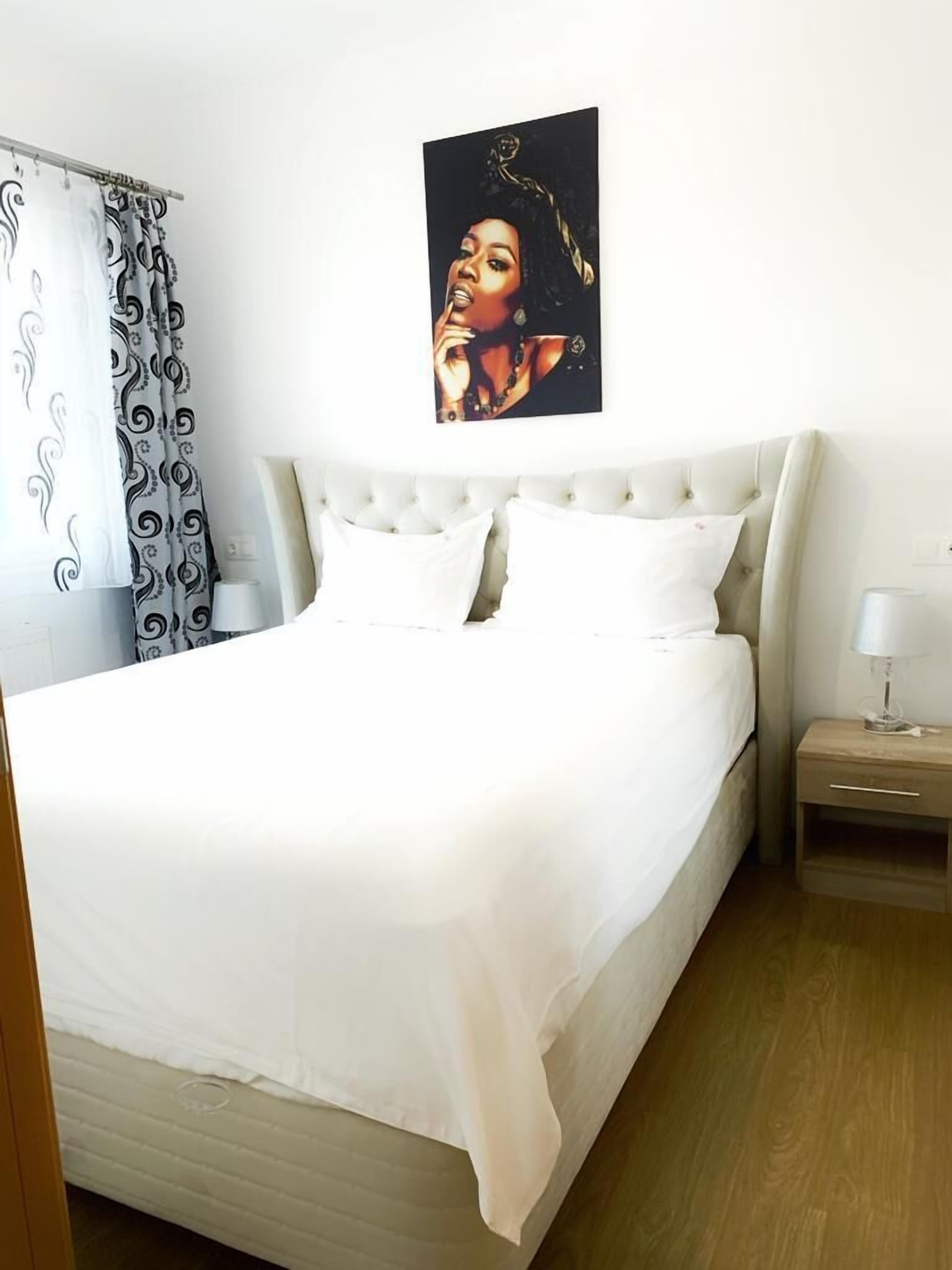 A neatly made bed with white bedding, a headboard, and a bedside table with a lamp.