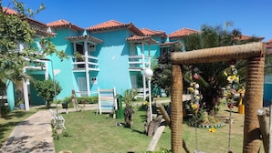 Un patio con un camino de piedra, un conjunto de columpios y un pequeño jardín con diversas plantas y flores.