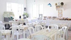 Un comedor con sillas y mesas blancas, un área de cocina con electrodomésticos y una decoración con delfines en la pared.