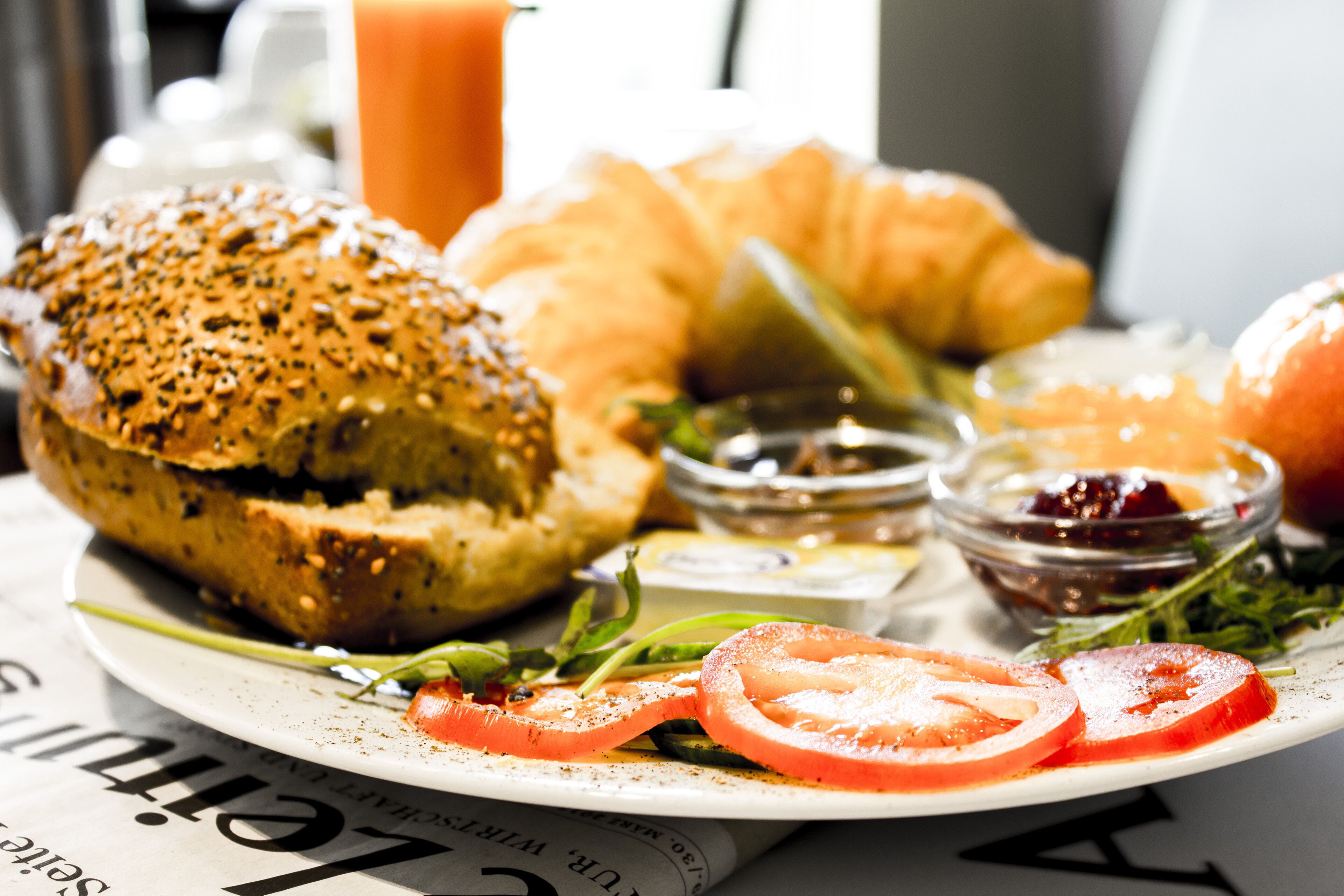 Een ontbijtplaats met een bagel, croissant, plakjes tomaat en kleine schaaltjes met toevoegingen.