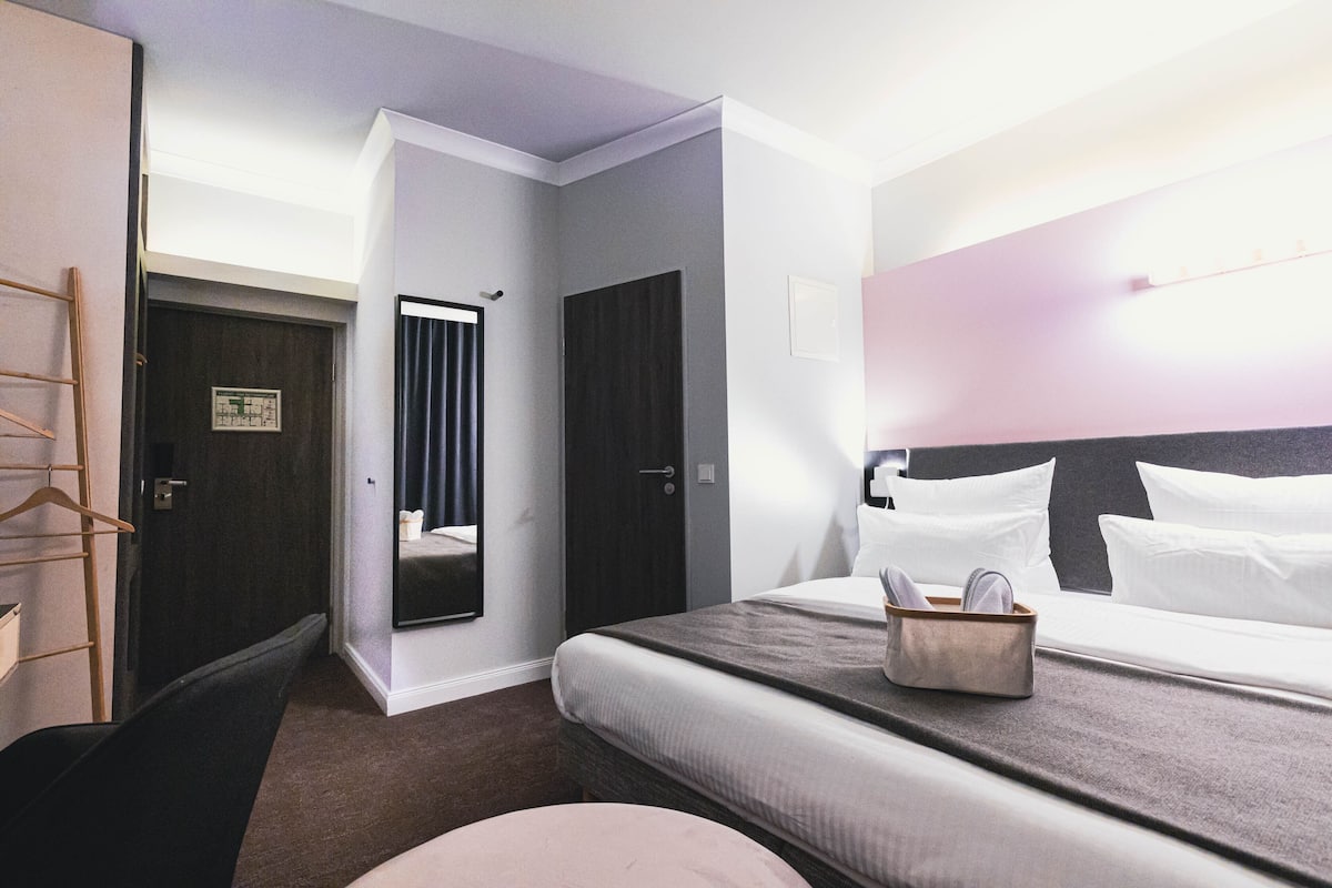 A hotel room with a bed, a bedside table with a lamp, a wardrobe, and a mirror.