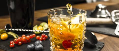 A glass with fruit and ice on a black slate, surrounded by berries and a bottle.